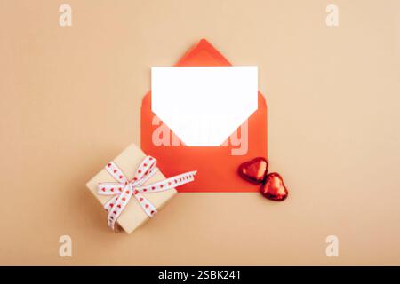 Red envelope and small gift box with heart-shaped decorations on a beige background, symbolizing love. Valentines day concept. Top view, flat lay, moc Stock Photo