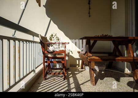 rustic wooden furniture on a sunlit balcony, a white domestic cat laying on a wooden chair, basking in the warm afternoon light. Pets at home behavior Stock Photo
