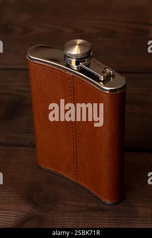 Stylish flask in a leather case on a wooden background. A classic accessory for traveling, outdoor recreation and a gift for a man Stock Photo