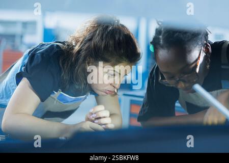 Qualified colleagues working on car in garage, checking radiator during routine maintenance. Teamworking auto repair shop mechanics inspecting vehicle parts using work light Stock Photo