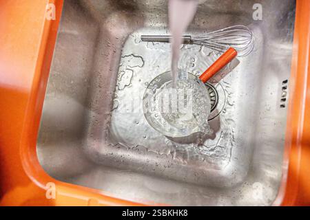 A good stream of hot water falling from the tap onto some containers inside a stainless steel sink Stock Photo