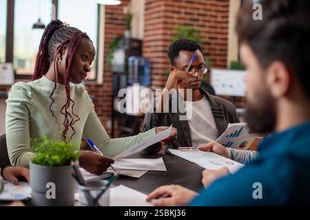 Selective focus on african american businessman and woman reviewing documents during a brainstorming session. Multiracial team members engaging in productive discussion with charts and notes. Stock Photo