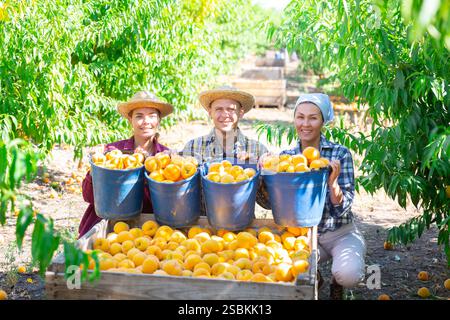Happy farmers posing with harvest of ripe peaches in orchard Stock Photo