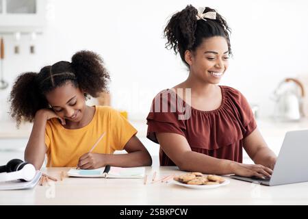 School girl doing homework by her working mother, kitchen interior Stock Photo