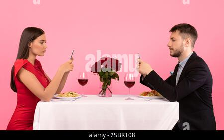 Couple Using Cellphones Sitting At Table Posing Over Yellow Background Stock Photo
