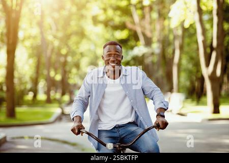 Positive black man having fun riding bike at city park Stock Photo