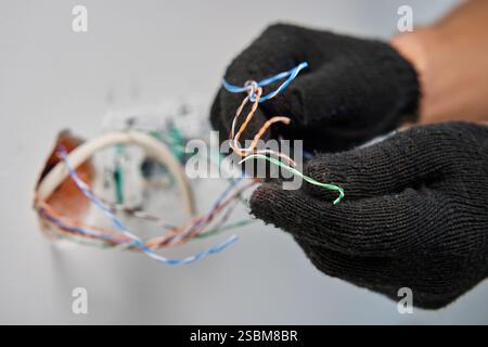 Technician wearing black gloves repairing network cables in wall socket. Close-up shot showing detailed wiring work and electrical maintenance Stock Photo
