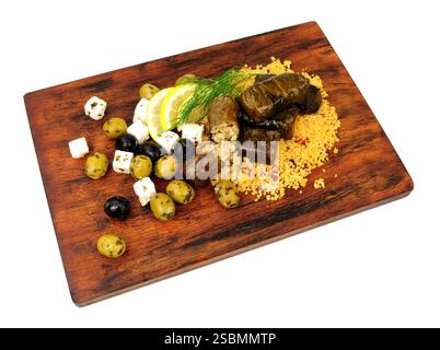 Rice stuffed vine leaves meal with couscous, Greek feta cheese and black olives on a wooden serving board isolated on a white background Stock Photo