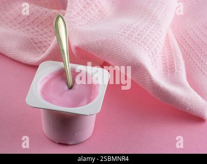 Pink yogurt cup with spoon on pink background with copy space Stock Photo