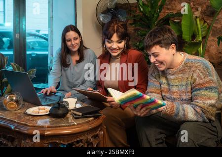 A diverse group of women and a non-binary person collaborating in a cozy cafe, working together in an inclusive and creative environment. Stock Photo