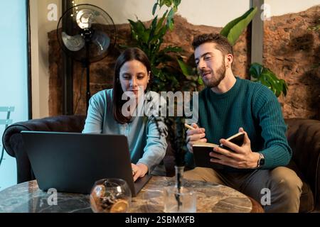 Young professionals discussing and collaborating on a laptop in a cozy café, representing teamwork, remote work, and creative brainstorming. Stock Photo