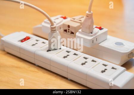 Many electrical plugs connected to a power white strip or extension block on wooden table. High-tech smart strip Stock Photo
