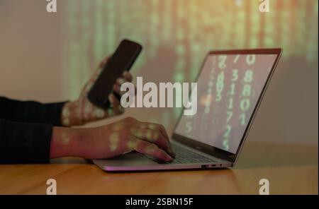 Hooded computer hacker use phone and stealing information with laptop. Selective focus. Stock Photo