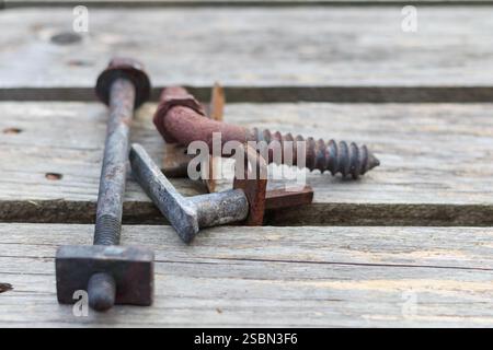 a rust-covered screw is visible on a wooden surface, with another screw and other objects in the background. Stock Photo