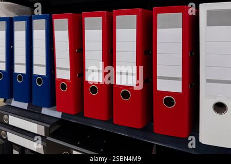 A row of neatly organized filing folders in vibrant colors sits on a shelf in an office environment. The folders are labeled and arranged for easy acc Stock Photo