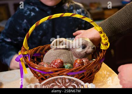 A brown ceramic rabbit rests in a woven basket alongside several intricately decorated eggs. The basket is adorned with yellow and purple ribbons. A p Stock Photo