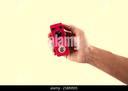 Male hand holding a pink guitar effects pedal isolated on light yellow background cutout Stock Photo
