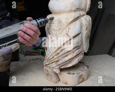 creative woodworking using a drill, cutting out a bird figure from solid wood using a construction hand tool, craftsman's work in a workshop Stock Photo