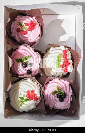 A arrangement of five cupcakes with pink and white frosting, adorned with red currants and blackberries, presented in a circular pattern inside a whit Stock Photo