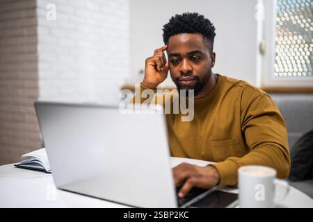 Concentrated African American freelancer using laptop while working at his comfortable home. Stock Photo