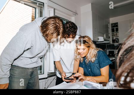 Male and female students sharing smart phone while studying together in college dorm Stock Photo