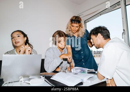 Young woman helping male friend while studying in college dorm Stock Photo