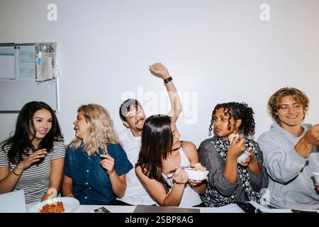 Group of cheerful male and female roommates enjoying while sitting together in college dorm room Stock Photo