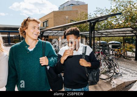 Young man wearing sunglasses and laughing while standing next to male friend at college campus Stock Photo