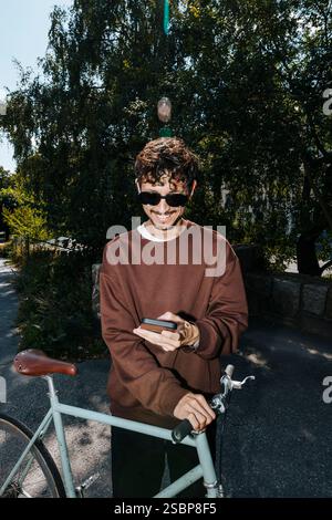 Smiling young man using smart phone while standing with bicycle at park Stock Photo