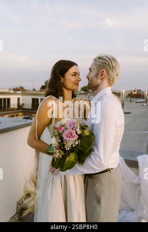 Romantic multiracial newlywed couple looking at each other while standing on rooftop Stock Photo