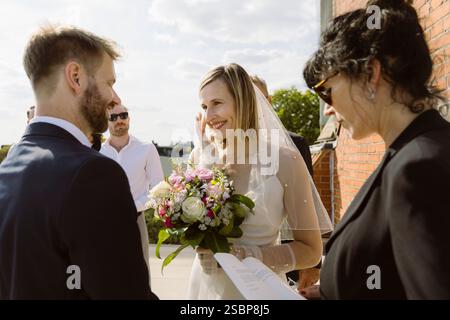 Loving couple looking at each other while standing near female minister during wedding ceremony Stock Photo