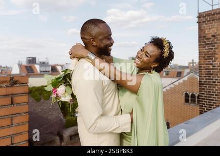 Happy bride with hands on shoulder of groom standing on rooftop Stock Photo