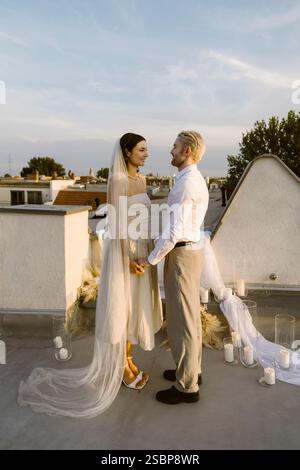 Smiling young married couple holding hands while standing on rooftop Stock Photo