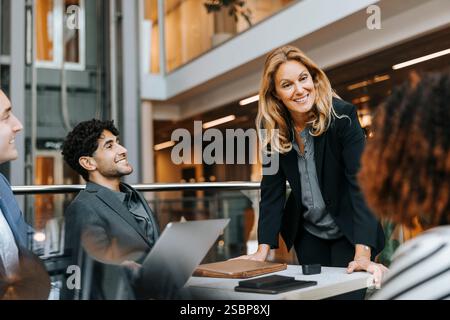 Smiling businesswoman leaning on table and discussing with colleagues in meeting at office Stock Photo