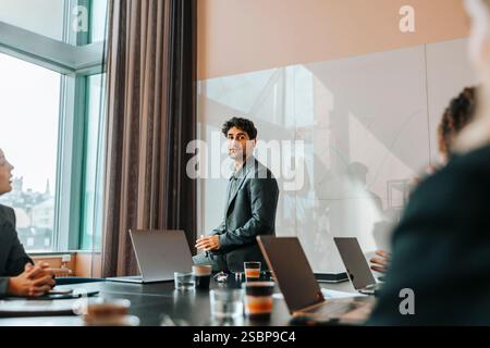Young male entrepreneur sitting on table in meeting with colleagues at office Stock Photo