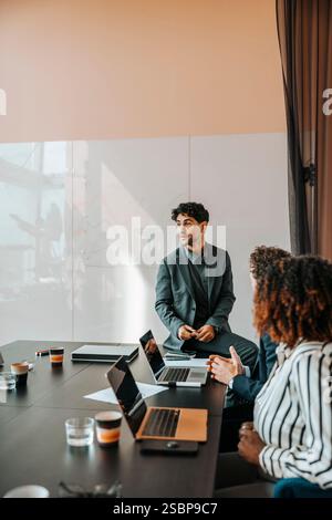 Male entrepreneur sitting on table and discussing with colleagues in board room at office Stock Photo