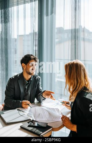 Male client talking with businesswoman while doing paperwork at office Stock Photo