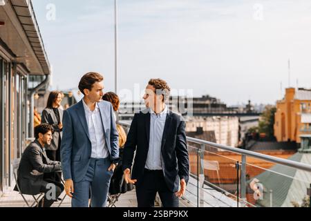 Male business professionals talking with each other while walking in balcony during coffee break Stock Photo