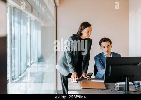 Businesswoman leaning on desk by male colleague using computer while sitting at office Stock Photo