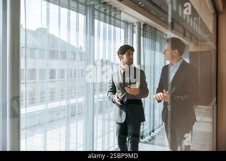 Male business professionals discussing while walking in office corridor seen through glass Stock Photo