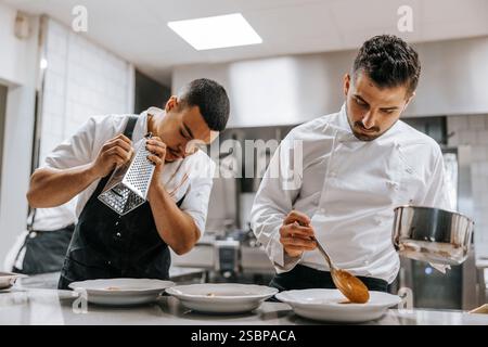 Young male chefs garnishing meal on kitchen counter in restaurant Stock Photo