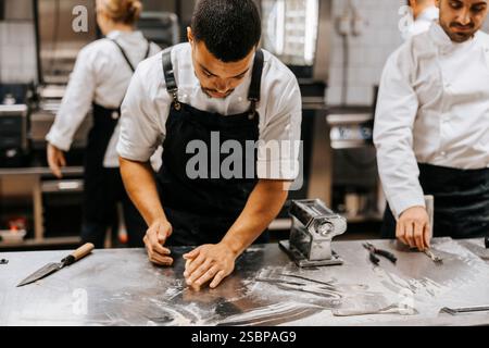 Young male chef kneading dough for pasta on kitchen counter in restaurant Stock Photo
