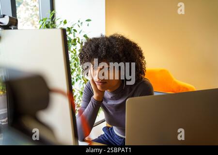 Bored young IT professional with curly hair working on desktop PC in tech hub Stock Photo
