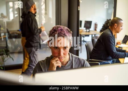 Focused non-binary computer programmer working in office Stock Photo