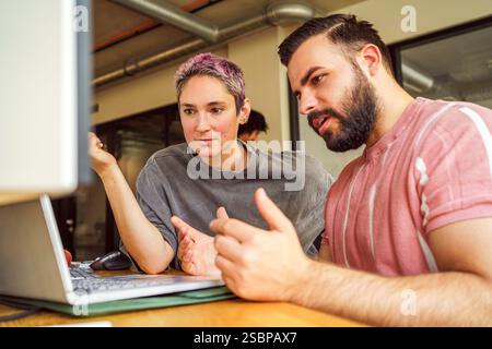 Male IT professional discussing with non-binary person in tech startup Stock Photo