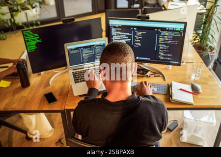 High angle rear view of male computer programmer sitting near desk in office Stock Photo