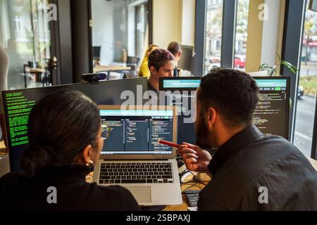 Rear view of male and female coding professional discussing over laptop while working in tech startup office Stock Photo