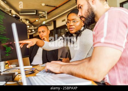 Female computer programmer pointing at desktop screen while discussing with male coworker in office Stock Photo