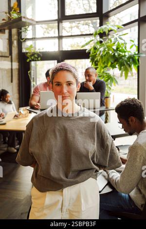 Portrait of non-binary business professional standing with hands behind back in office Stock Photo