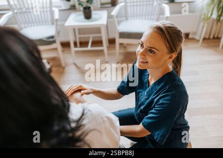 High angle view of smiling healthcare worker crouching near female patient at care home Stock Photo